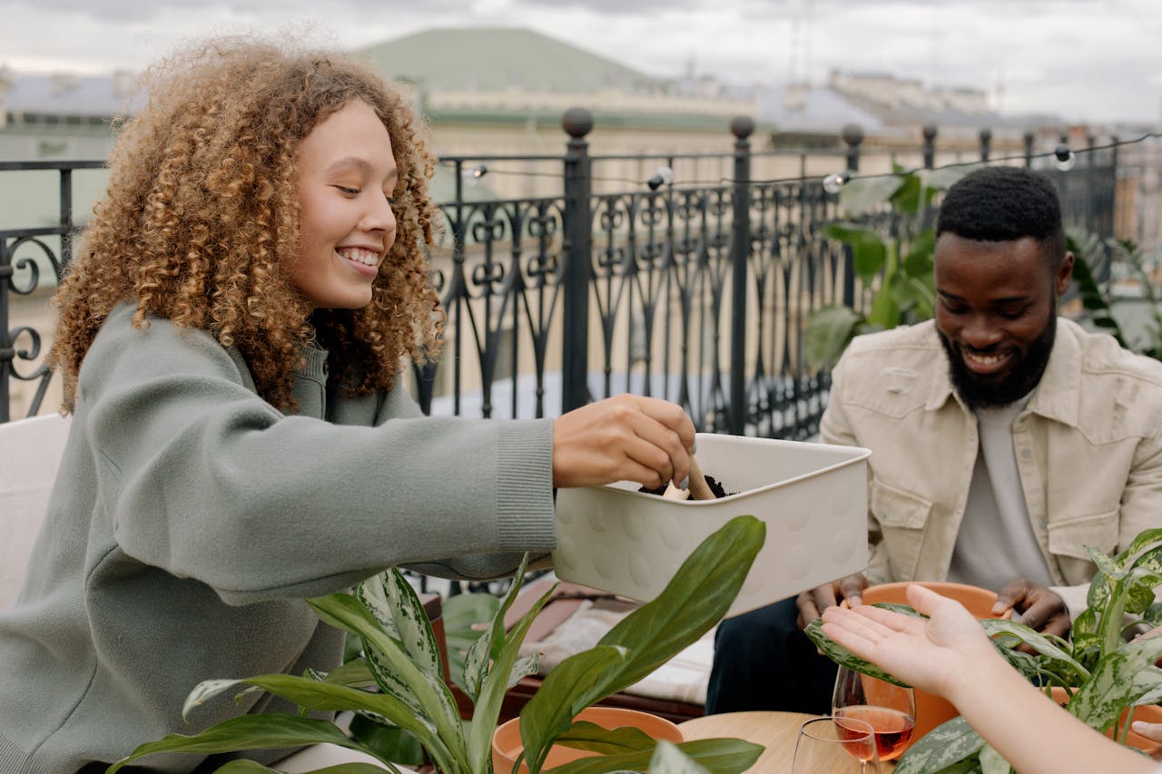 Two friends enjoying rooftop gardening with potted plants and soil, creating a joyful atmosphere.